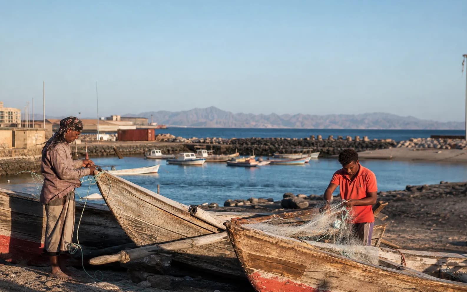 Two fishers preparing nets beside wooden boats on the Red Sea coast