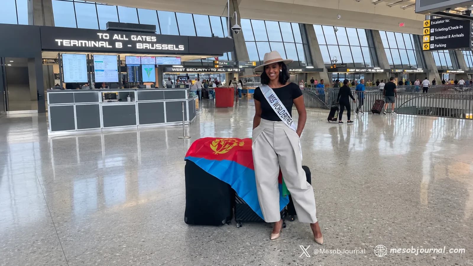 Miss World Eritrea beside luggage with Eritrean flag; background digitally expanded.